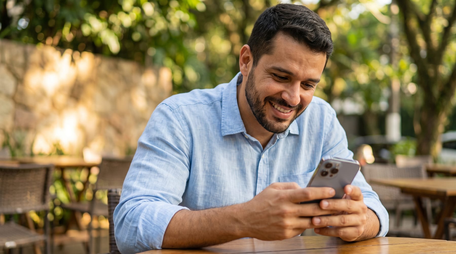 Man smiling with his phone in hand, at a coffee shop table